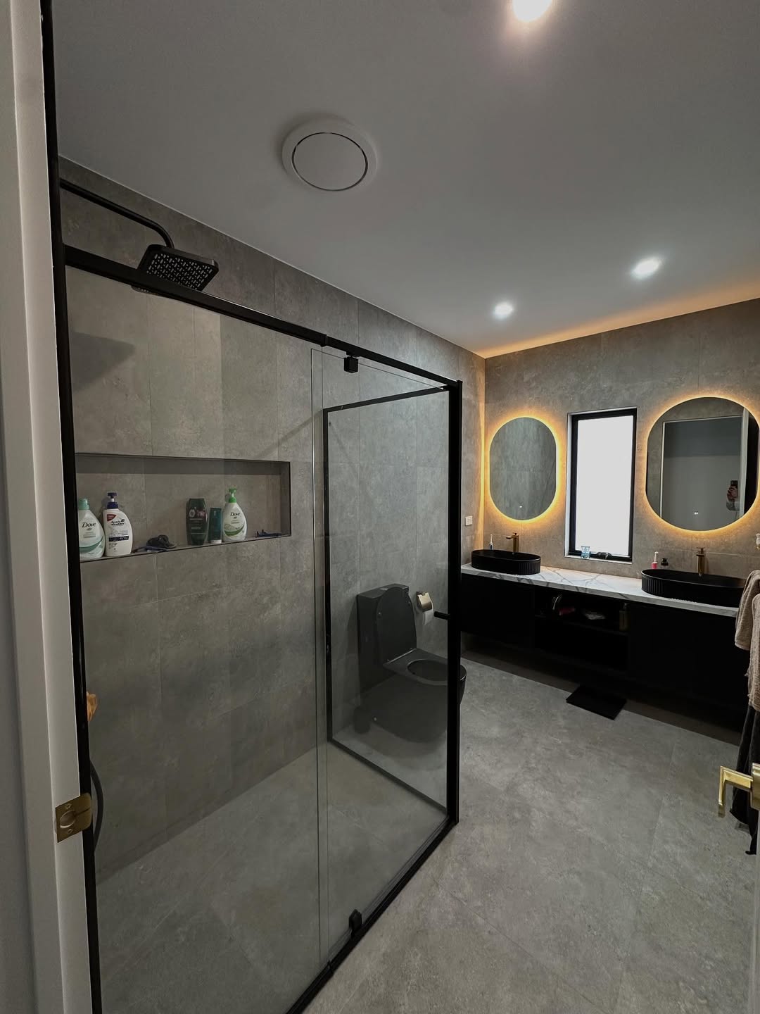 Dark themed bathroom with double vanity and LED mirrors